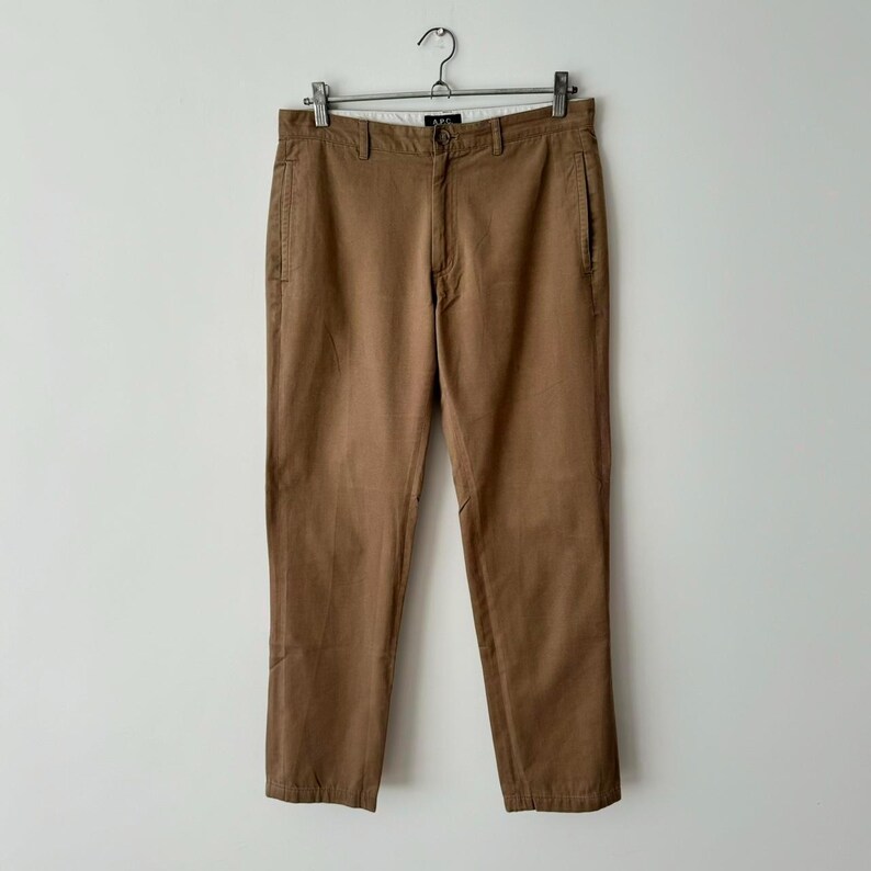 May include: Brown cotton pants with a straight leg fit. The pants have a zipper fly and belt loops.