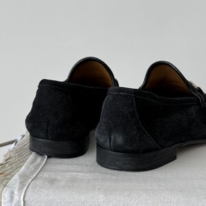 Pu&ograve; includere: Un paio di mocassini in pelle scamosciata nera con suola in cuoio. I mocassini hanno una punta a punta e un design slip-on.