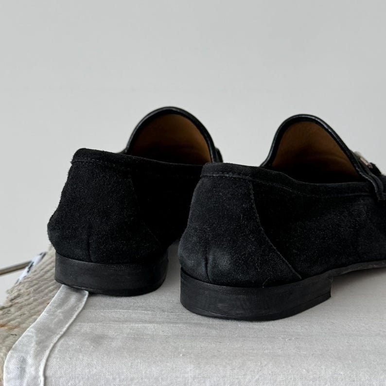 Pu&ograve; includere: Un paio di mocassini in pelle scamosciata nera con suola in cuoio. I mocassini hanno una punta a punta e un design slip-on.
