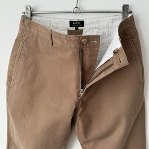 May include: A pair of brown cotton twill pants with a zipper fly and a button closure. The pants have a single back pocket and a label that reads "A.P.C."