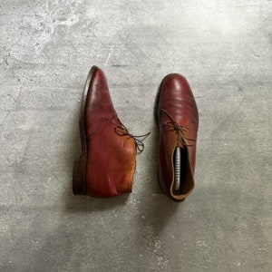 May include: A pair of brown leather ankle boots with laces. The boots have a slightly distressed look and are made of a soft, supple leather.