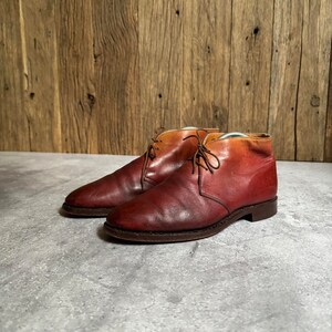 May include: A pair of brown leather ankle boots with a gradient color effect, transitioning from a lighter brown to a darker red. The boots have laces and a rounded toe.