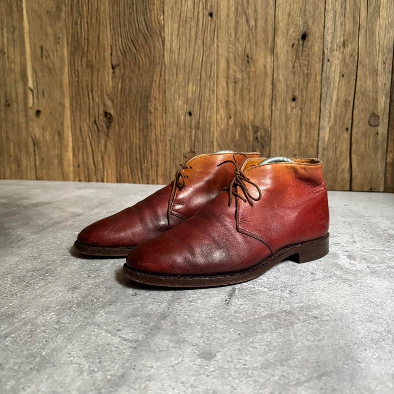 May include: A pair of brown leather ankle boots with a gradient color effect, transitioning from a lighter brown to a darker red. The boots have laces and a rounded toe.