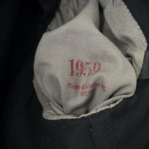 Puede incluir: Primer plano de una etiqueta de tela gris con el texto "1959" y "Rieder & Schaffer, Berl&iacute;n" en letras rojas.