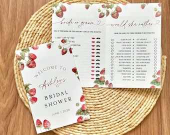 May include: Bridal shower game cards with strawberry illustrations. One card reads "Welcome to Ashley's Bridal Shower June 1, 2026." The other cards have questions like "Bride or Groom?" and "Would She Rather?" on a woven mat.