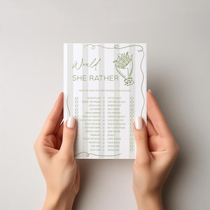 May include: A white card with green text and a floral illustration, held by two hands. The card reads "Would She Rather" with a list of choices below, such as "Sleep in Late" and "Get Up Early."