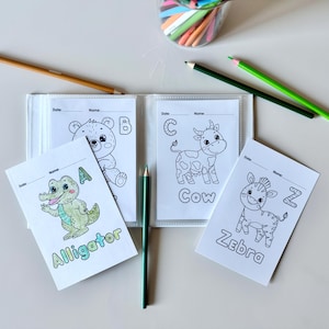 May include: A set of four coloring pages featuring animals and letters. The pages are in a binder and include an alligator, a bear, a cow, and a zebra. Each page has a letter and the name of the animal.