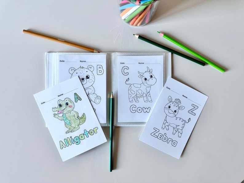 May include: A set of four coloring pages featuring animals and letters. The pages are in a binder and include an alligator, a bear, a cow, and a zebra. Each page has a letter and the name of the animal.