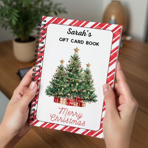May include: A spiral-bound gift card book with a white cover featuring a Christmas tree design. The cover has red and white candy cane stripes around the edges. The text "Sarah's GIFT CARD BOOK" and "Merry Christmas" are displayed on the cover.