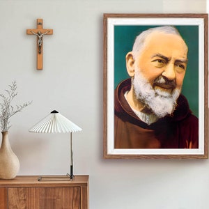 May include: A framed portrait of a man with a white beard and brown robes. The man is smiling and looking to the right. The background is a green color.