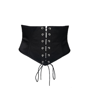May include: Black corset with a lace-up front. The corset features silver grommets and a tie closure. The garment is made of a smooth, matte fabric and has a structured design. The corset is designed to cinch the waist.