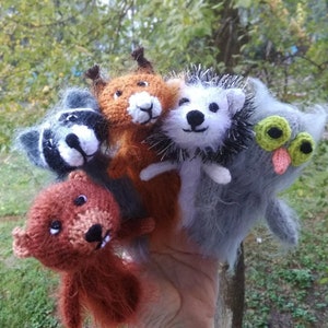 May include: Five finger puppets made of knitted fabric. The puppets are a raccoon, a fox, a hedgehog, a bear, and an owl. The puppets are all wearing different colors and have different facial expressions.