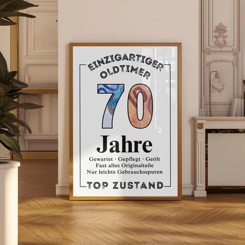 May include: Framed print with the text "EINZIGARTIGER OLDTIMER 70 Jahre" in black and white. The number 70 is in blue and orange. The print has a gold frame and is displayed against a white wall.
