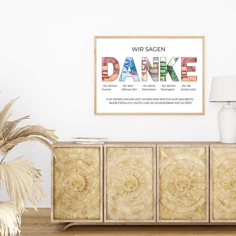 May include: A framed print with the German word "DANKE" in large, colorful letters. The word is composed of images of money. The print includes additional text in German, and is displayed above a wooden cabinet.