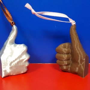 May include: Two thumbs up ornaments, one silver and one brown, with ribbon loops for hanging.