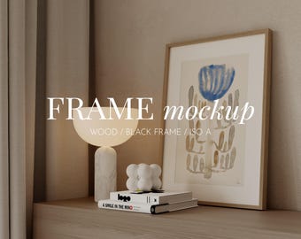 May include: A black framed picture with a watercolor painting of a blue flower with brown stems. The picture is on a wooden shelf with a white lamp and books.