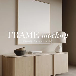 以下が含まれることがあります： 「FRAME mockup」のテキストが入った、大きな額入りのキャンバスが特徴のミニマリストなインテリアシーン。 大理石の天板が付いた木製のキャビネットには、装飾的なボウル、本、ランプが置かれています。 ランプは白いシェードとユニークなベースを備えています。
