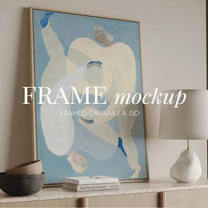 Puede incluir: Un lienzo enmarcado con una pintura abstracta en tonos azules y blancos. La obra presenta figuras en movimiento. El texto "FRAME mockup" se muestra en el lienzo. Una lámpara blanca y cuencos decorativos están sobre una superficie de madera.