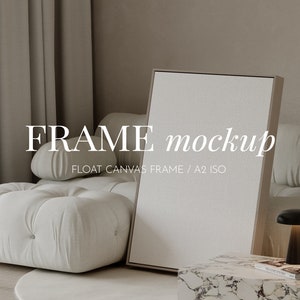 Könnte beinhalten: Ein weißer Leinwandrahmen-Mockup in einer Wohnzimmerumgebung. Der Rahmen lehnt an einem weißen Sofa mit einer schwarzen Lampe auf einem Marmor-Beistelltisch. Der Text "FRAME mockup" und "FLOAT CANVAS FRAME / A2 ISO" wird unterhalb des Rahmens angezeigt.