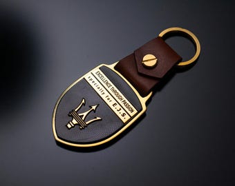 May include: A black and gold keychain with a brown leather strap. The keychain features a shield design with the text "EXCELLENCE THROUGH PASSION" and "specially for E.J.S." The emblem includes a trident symbol.