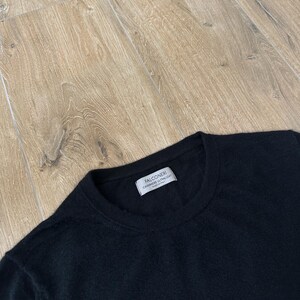 Puede incluir: Un su&eacute;ter negro de manga larga con cuello redondo. Una etiqueta rectangular blanca est&aacute; cosida en el interior del cuello, con el texto FALCONERI, CASHMERE ULTRALIGHT y MADE IN ITALY en letras negras. La prenda tiene una textura de punto fino y ligero.