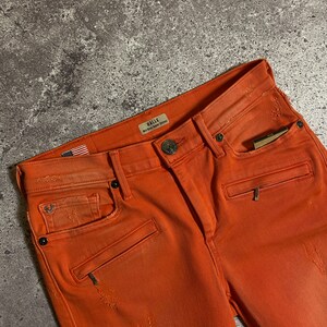 May include: Orange distressed denim jeans with a small American flag patch and a Halle label that reads "Red Bird Super Skinny".