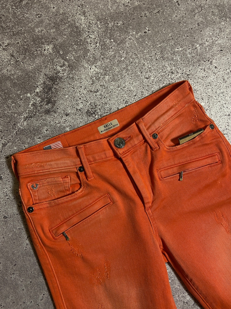 May include: Orange distressed denim jeans with a small American flag patch and a Halle label that reads "Red Bird Super Skinny".