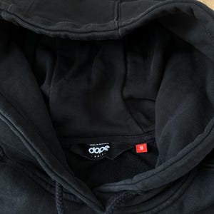 May include: Black hooded sweatshirt with a drawstring and a front pocket. The label inside the collar reads "dope" and "MADE IN PORTUGAL". The size tag is red and marked "M". The word "SNOW" is visible at the bottom of the sweatshirt.