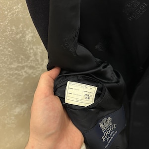 May include: A navy blue blazer with a satin lining. The interior features a label with the brand name "Boggi Milano" and a fabric composition tag. The blazer's lining is imprinted with the Boggi Milano logo.