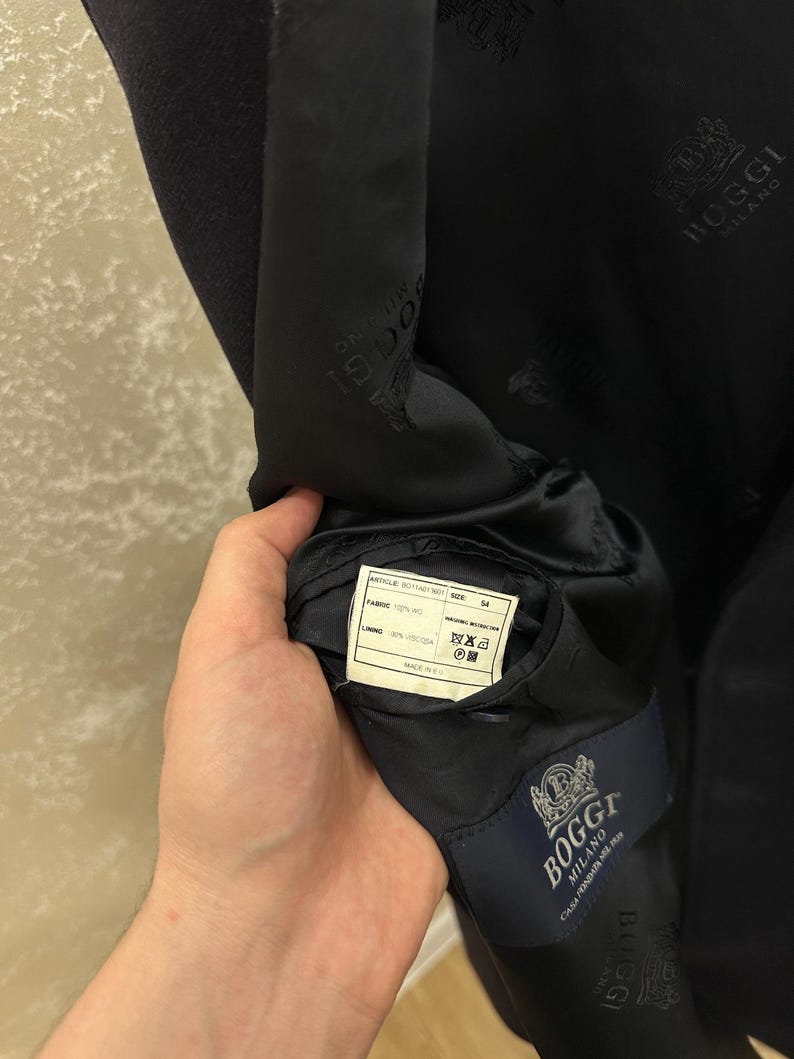 May include: A navy blue blazer with a satin lining. The interior features a label with the brand name "Boggi Milano" and a fabric composition tag. The blazer's lining is imprinted with the Boggi Milano logo.