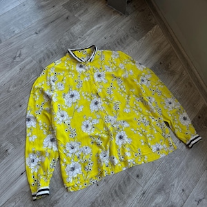 Könnte beinhalten: Ein gelbes Langarmhemd mit weißem Blumenmuster und schwarz-weißem Besatz an Kragen und Manschetten.