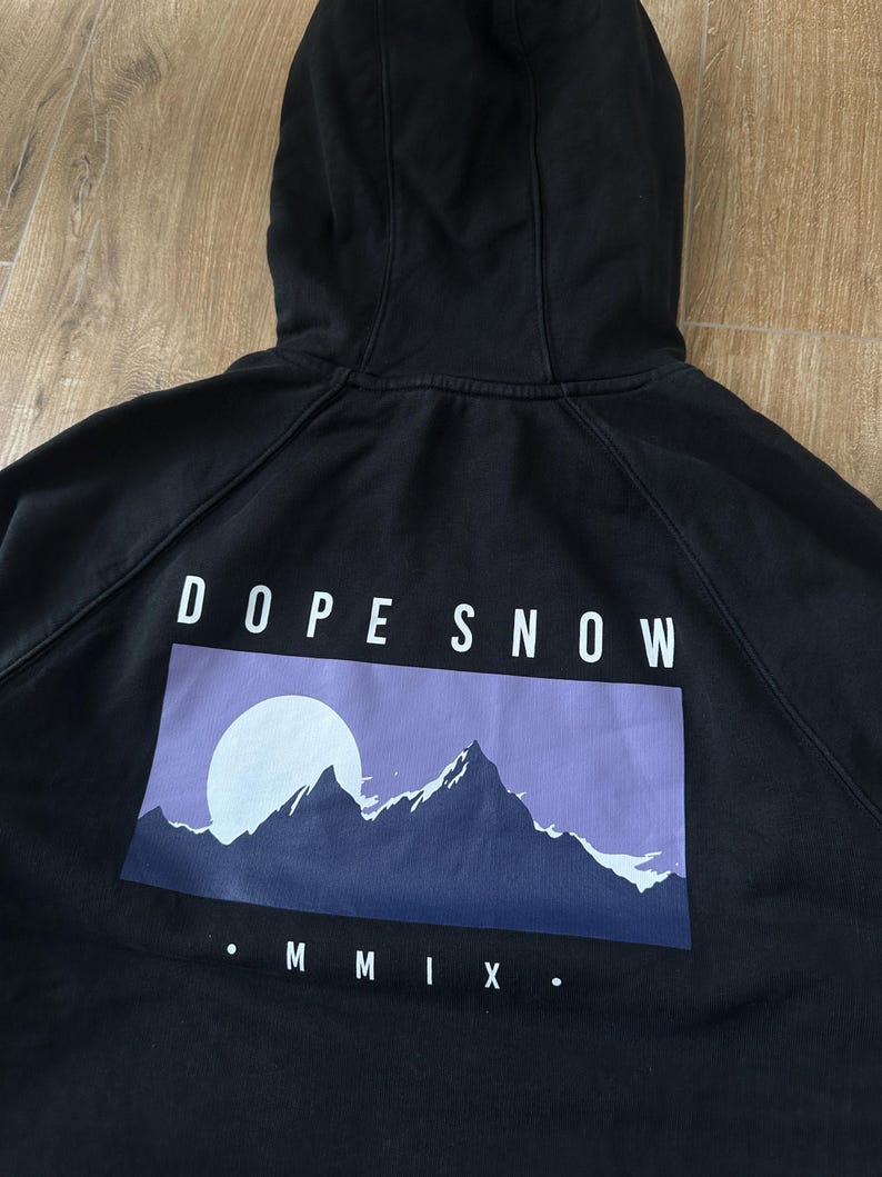 May include: Black hooded sweatshirt with the text "DOPE SNOW" above a graphic of a mountain range and a full moon. The graphic is in shades of purple and blue. The Roman numeral "MMIX" is below the graphic.