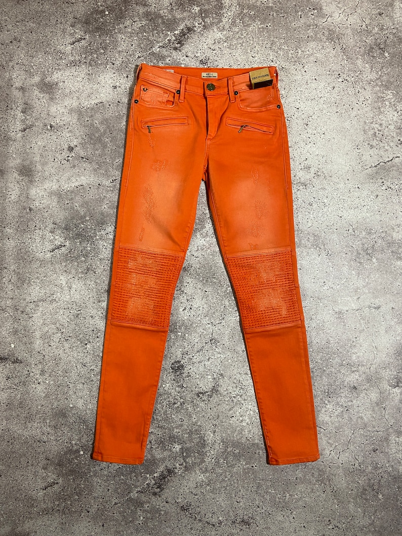 May include: Orange skinny jeans with zipper details and knee pads.