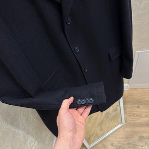 May include: A navy blue blazer with three buttons on the sleeve and three on the front. The blazer has two pockets and a notched lapel. The fabric appears to be a wool blend. The blazer is a classic style.