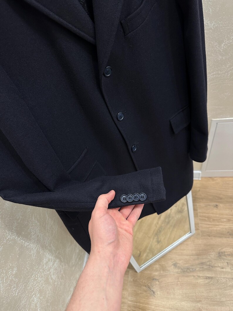 May include: A navy blue blazer with three buttons on the sleeve and three on the front. The blazer has two pockets and a notched lapel. The fabric appears to be a wool blend. The blazer is a classic style.