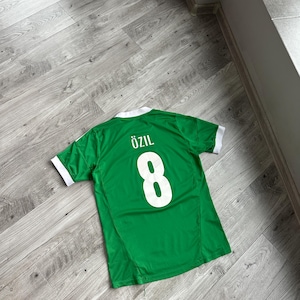 May include: A green soccer jersey with white trim and the name "Özil" and the number "8" on the back.