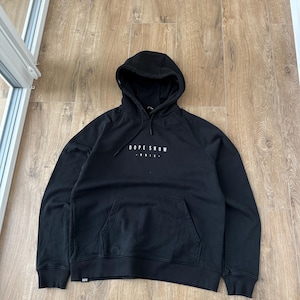 May include: Black hooded sweatshirt with the text "DOPE SNOW" in white across the chest. The sweatshirt has a kangaroo pocket and a drawstring hood. The garment is made of a soft material.
