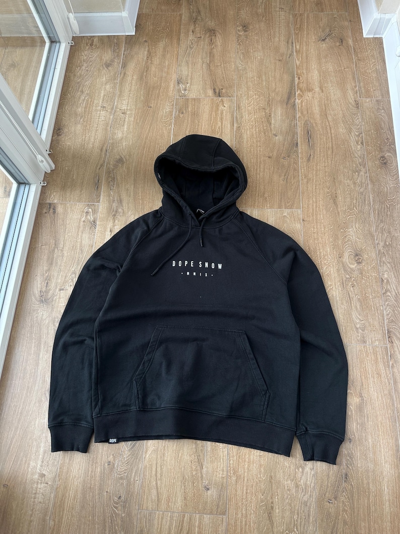 May include: Black hooded sweatshirt with the text "DOPE SNOW" in white across the chest. The sweatshirt has a kangaroo pocket and a drawstring hood. The garment is made of a soft material.