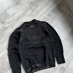 May include: Black athletic long-sleeve shirt with textured panels and ribbed cuffs. The shirt features the text "X-BIONIC INVENT" and a geometric design on the back. The shirt is designed for athletic activities.