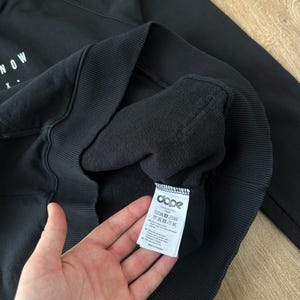 May include: Black hooded sweatshirt with the word "NOW" printed in white on the front. The sweatshirt has a ribbed hem and cuffs. A tag with the brand "dope" is visible.