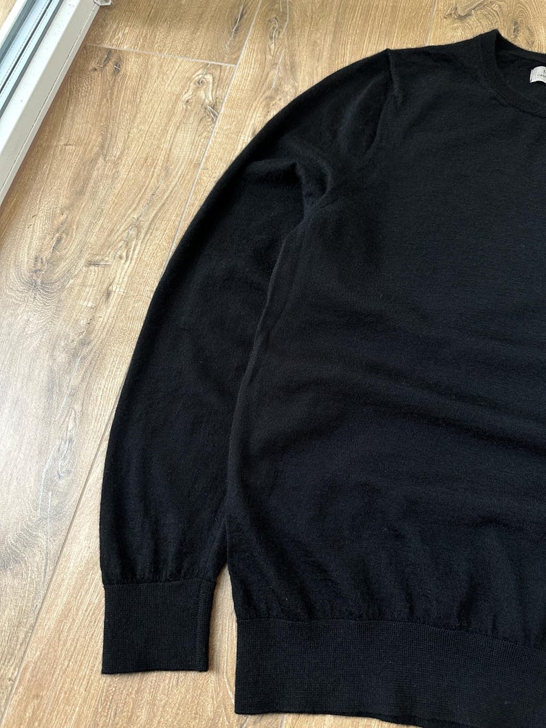 Puede incluir: Un su&eacute;ter negro de manga larga con cuello redondo cl&aacute;sico, pu&ntilde;os acanalados en las mu&ntilde;ecas y un dobladillo acanalado. La prenda est&aacute; confeccionada con un tejido de punto fino y muestra un color negro profundo y uniforme en toda la pieza.