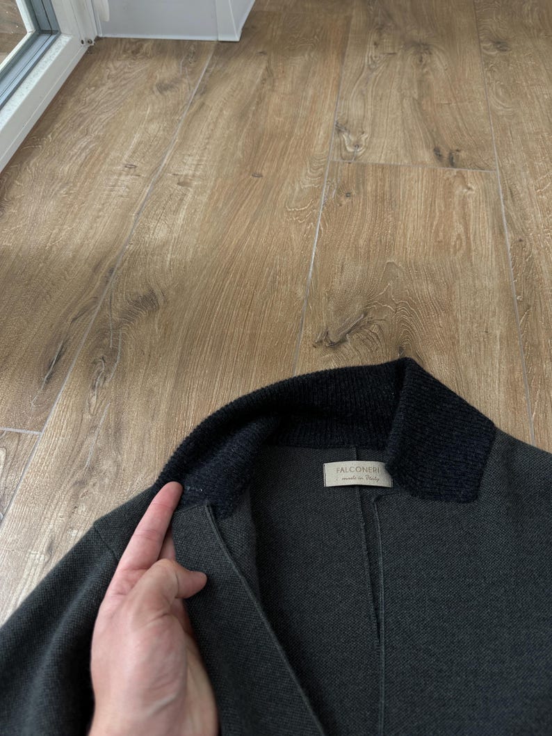 Op de afbeelding: Een donker antracietgrijze jas met een contrasterende zwarte kraag van geribd breiwerk. Het kledingstuk heeft een wit binnenlabel met de tekst Falconeri made in Italy bij de halslijn en toont een constructie van gestructureerde stof.
