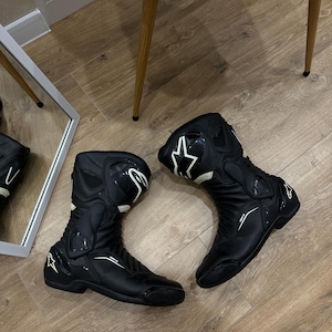Peut inclure: Une paire de bottes de moto noires Alpinestars avec des accents de logo blancs, une protection de cheville renforcée et un design structuré et élégant. Ces bottes mi-mollet comprennent des panneaux moulés et une semelle durable.