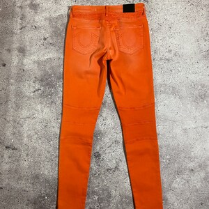 May include: Orange skinny jeans with a True Religion logo on the back pockets.