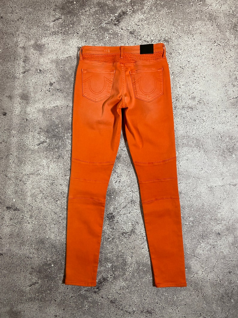 May include: Orange skinny jeans with a True Religion logo on the back pockets.
