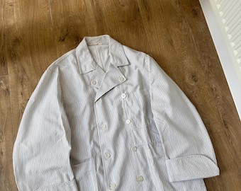 May include: A double-breasted jacket featuring a white and navy blue vertical pinstripe pattern. The garment includes a notched lapel, long sleeves with wide cuffs, and six light-colored buttons arranged in two columns on the front panel.