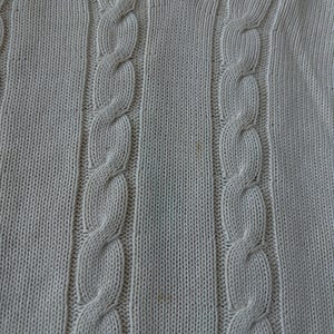 Puede incluir: Su&eacute;ter de punto trenzado color crema con cuello en V. El su&eacute;ter presenta un dise&ntilde;o de punto trenzado texturizado en la parte delantera y un ribete a rayas en el cuello. La prenda de punto es de color neutro, adecuada para varios conjuntos.