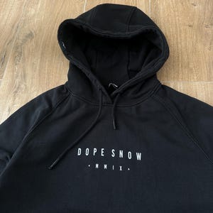 May include: Black hooded sweatshirt with the text "DOPE SNOW" and "MMIX" in white. The sweatshirt has a drawstring hood and a kangaroo pocket. The fabric appears to be a soft, medium-weight material.
