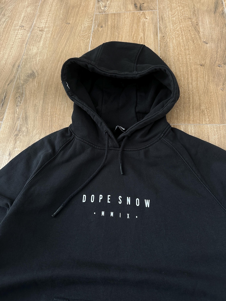 May include: Black hooded sweatshirt with the text "DOPE SNOW" and "MMIX" in white. The sweatshirt has a drawstring hood and a kangaroo pocket. The fabric appears to be a soft, medium-weight material.