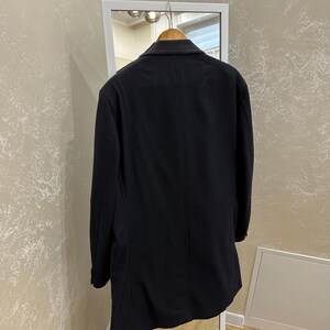 May include: A dark navy blue coat hanging on a wooden hanger inside a white framed mirror. The coat is a classic style with a tailored fit and a single-breasted design. The coat is made of a smooth, solid fabric.